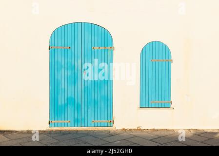Chiusa porta in legno blu e serranda su una facciata bianca nel centro storico di Alghero sopra le mura della fortezza nel caldo sole della sera, Sardegna, Italia Foto Stock