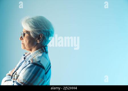Ritratto di profilo di una donna anziana europea pensando alla sua malattia medio closeup copia studio shot blu sfondo sanitario concetto. Foto di alta qualità Foto Stock
