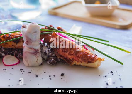 Polpo alla griglia con fagioli neri su un piatto bianco in un ristorante a Menton, Francia. Squisita cucina francese. Riposati sulla costa azzurra. Foto Stock