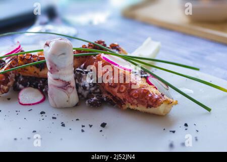 Polpo alla griglia con fagioli neri su un piatto bianco in un ristorante a Menton, Francia. Squisita cucina francese. Riposati sulla costa azzurra. Foto Stock