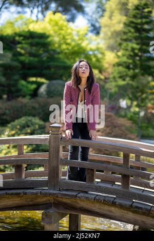 Giovane donna in abiti casual su un ponte su un laghetto giapponese Koi Foto Stock