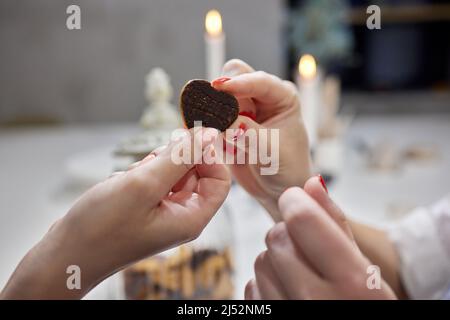 Primo piano di forti mani maschili che tengono piccole mani di bambini con biscotti a forma di cuore all'interno, simbolo di amore, famiglia e legame Foto Stock