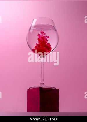 Bicchiere di vino su un cubo con colorante rosso che si scioglie in acqua Foto Stock