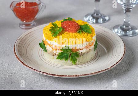 Insalata di soffusa Mimosa con pesce in scatola, patate, formaggio, carote e uova, guarnita con caviale rosso e foglie di prezzemolo su sfondo grigio Foto Stock
