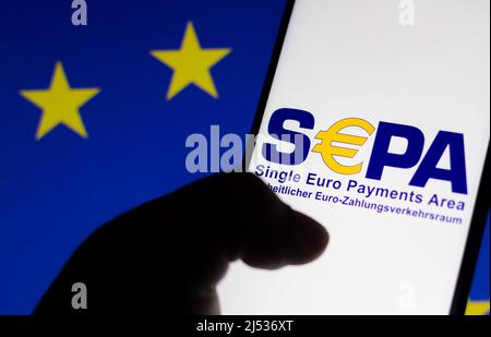 In questa foto è mostrato il logo Single Euro Payments Area (SEPA) visualizzato su uno smartphone e sullo sfondo la bandiera dell'Unione europea (UE). Foto Stock