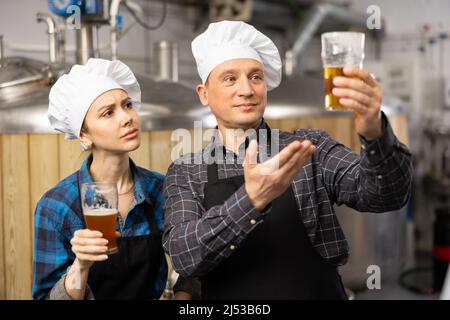 I produttori di birra interessati, maschi e femmine, che esaminano la qualità della birra in birrificio Foto Stock