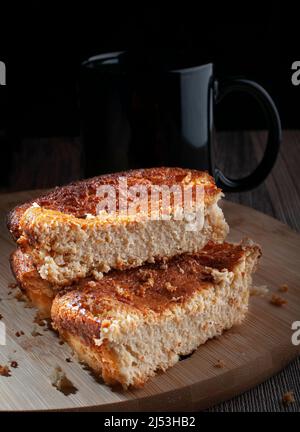 Pezzi fatti in casa di torta di mais su un bordo di taglio di legno rotondo con uno sfondo nero, con una tazza nera di caffè in fondo. Foto Stock