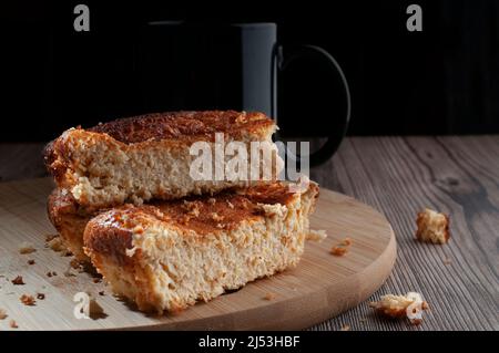 Pezzi fatti in casa di torta di mais su un bordo di taglio di legno rotondo con uno sfondo nero, con una tazza nera di caffè in fondo. Foto Stock