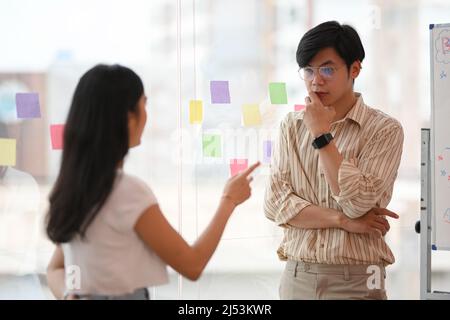 Un serio lavoratore maschile asiatico si è concentrato ad ascoltare le sue colleghe femminili spiegare i problemi e trovare una soluzione per risolverli. Foto Stock