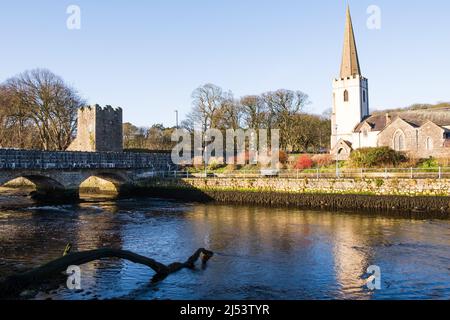 Ponte sul fiume a Glenarm nella contea di Antrim, Irlanda del Nord, con la chiesa di San Patrizio illuminata dal sole di mattina presto. Foto Stock