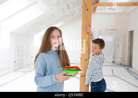 Fratello e sorella sono sul sito di costruzione della loro nuova camera loft appartamento con carte colore e la regola pieghevole e misurare tutto Foto Stock