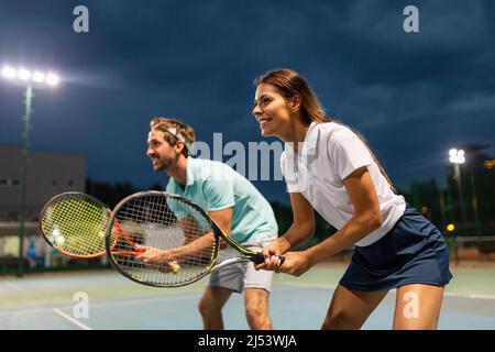 Concetto di persone di sport di tennis. Giocatore doppio misto che colpisce la palla da tennis con il partner in piedi vicino alla rete Foto Stock