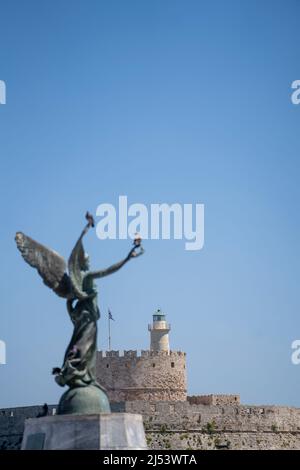 Fortezza di San Nicola nel porto di Mandraki in primo piano e nella facciata Angel Statua della Vittoria . Foto Stock