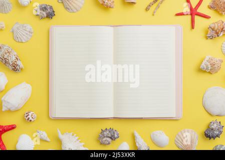 Apri un notebook vuoto, circondato da conchiglie e stelle marine per una presentazione promozionale. Vista dall'alto, composizione di posa piatta su superficie gialla Foto Stock