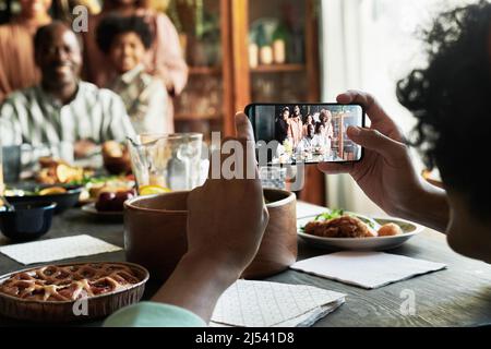 Giovane ragazzo che fa foto della sua grande famiglia sul telefono cellulare durante la cena di festa a casa Foto Stock