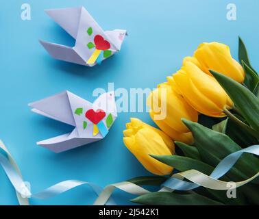 Tulipani gialli e uccelli di carta origami su sfondo blu. Colori della bandiera Ucraina. Sostegno all'Ucraina. Foto Stock