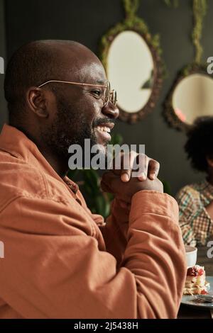 Vista laterale dell'uomo africano in occhiali sorridenti e godendosi il tempo con la sua famiglia a cena di famiglia Foto Stock