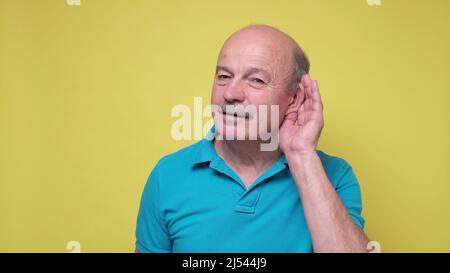 Uomo anziano che cerca di ascoltare le ultime notizie tenendo la mano vicino all'orecchio. Foto studio. Foto Stock
