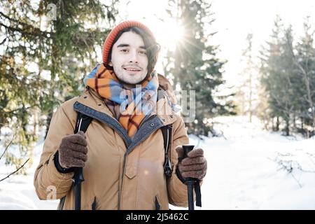 Ritratto di giovane gioioso che indossa abiti eleganti con zaino in piedi da qualche parte in montagna nella soleggiata giornata invernale Foto Stock