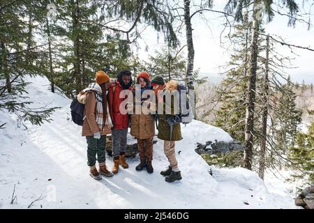 Visualizzazione ad alto angolo ampio scatto di giovani amici multietnici che si uniscono in montagna scegliendo il percorso utilizzando l'app mappa sullo smartphone Foto Stock