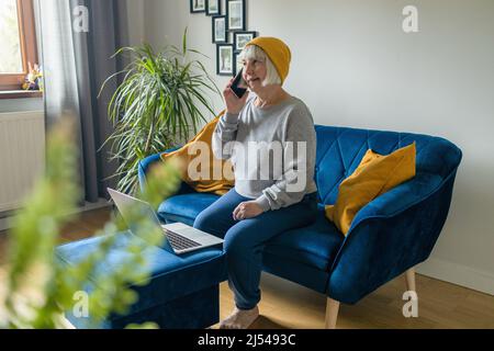 Felice anziano matura 50s anziano donna che chiacchiera al telefono, seduto al tavolo a casa, parlando con i colleghi, lavorando a casa, spiegando, facendo Foto Stock