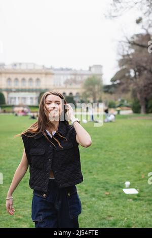 giovane donna allegra in giacca senza maniche nel parco verde Foto Stock