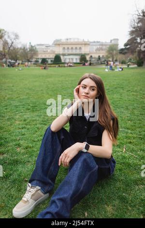 giovane donna premurosa in giacca senza maniche seduta sul prato Foto Stock