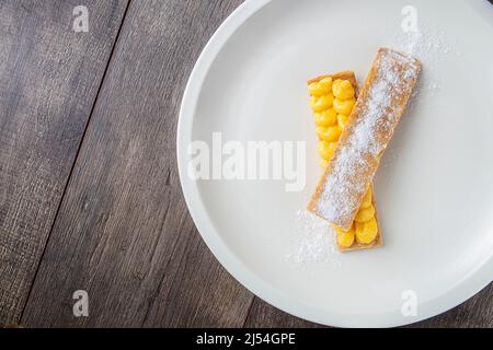 Pasta sfoglia pantxineta con crema al limone e zucchero a velo su un piatto bianco su un rustico sfondo di legno. Dessert tipico del Paese Basco spagnolo Foto Stock