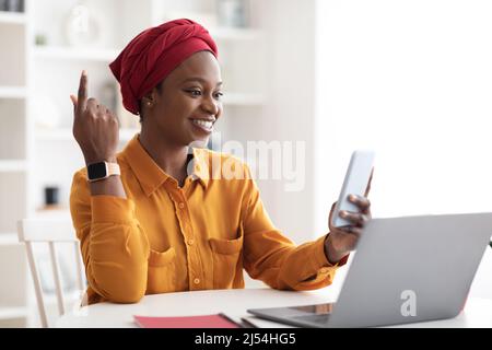 Donna d'affari afro-americana positiva che usa smartphone e laptop Foto Stock