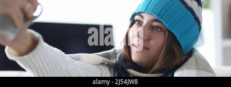 Giovane donna in cappello e plaid con brividi prende una tazza di medicina Foto Stock