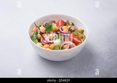 Cibo vegano sano e gustoso. Insalata di ceci con prezzemolo, pomodori ciliegini, cipolla, cetrioli e olive verdi su sfondo grigio di cemento Foto Stock