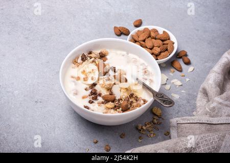 Granola con yogurt, banana fresca e noci di mandorle per una colazione sana su fondo di cemento grigio Foto Stock