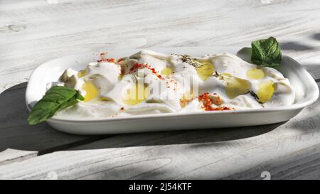 Un piatto Labneh guarnito con erbe, peperoni caldi e menta su un tavolo di legno. Foto Stock