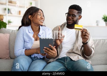 Coppia nera con tablet e carta bancaria a casa Foto Stock