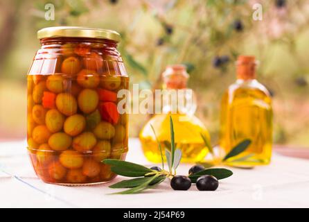 vasetto di vetro di olive in aceto, olio e olive su tavola in un campo d'oliva Foto Stock