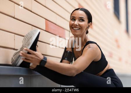 Felice giovane atleta araba con cuffie che si allungano per le gambe in allenamento Foto Stock