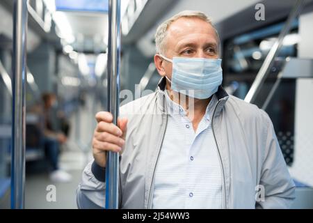 I passeggeri maturi indossano una maschera protettiva in un'auto metropolitana sotterranea Foto Stock