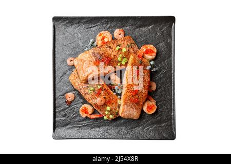 Bistecche di salmone fritte con gamberi fritti, su un piatto nero, isolarle su bianco Foto Stock