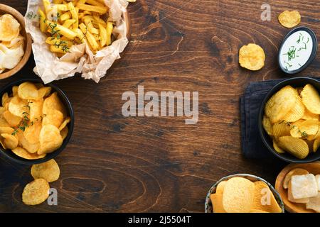 Cibo o spuntini malsani. Tutti i classici spuntini di patate con arachidi, anelli di popcorn e cipolle e pretzel salati in piatti da ciotola su vecchio sfondo di legno. Foto Stock