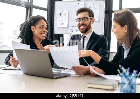 Partner aziendali creativi di successo che lavorano a un progetto. I colleghi multirazziali stanno brainstorming sulla strategia insieme, seduti in un ufficio moderno, studiando documenti, usando il laptop, discutendo, sorridendo Foto Stock