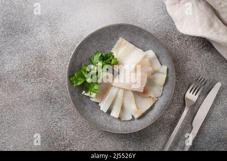 Deliziose fette di halibut affumicate servite con prezzemolo su sfondo grigio. Vista dall'alto. Spazio di copia. Foto Stock