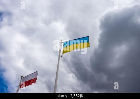 Le bandiere polacche e ucraine ondano sullo sfondo del cielo nuvoloso e drammatico. Foto scattata in giornata, cielo pieno di nuvole. Foto Stock