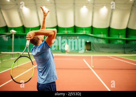 Istruttore o allenatore che insegna a giocare a tennis su un campo al coperto Foto Stock
