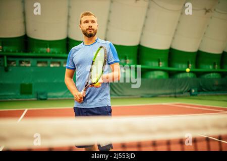 Istruttore o allenatore che insegna a giocare a tennis su un campo al coperto Foto Stock