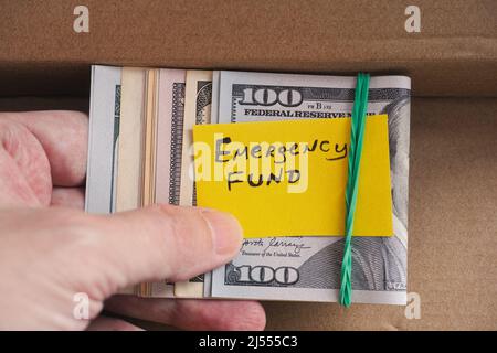 Un uomo che tiene alcune fatture del dollaro con una nota gialla della carta che dice il fondo di emergenza su loro nella sua mano. Primo piano. Foto Stock