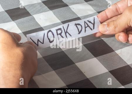 Giorno di lavoro, scritto su un pezzo di carta tenuto dalle mani di un uomo. Foto Stock