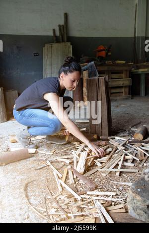 foto verticale di una ragazza che raccoglie legna da ardere da terra che ha tagliato con un hatchet. lavoro degli uomini fatto da una donna. empowerment. Spazio di copia Foto Stock