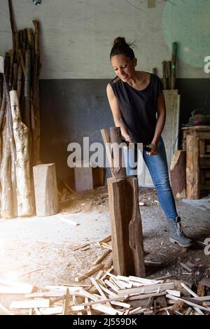 fotografia verticale di una giovane donna che trita legno per fare fuoco con un sorriso sul suo volto. emancipazione femminile. uguaglianza sul posto di lavoro. Spazio di copia Foto Stock