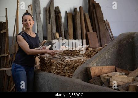 giovane donna bruna sorridente come lei impila legna da ardere tagliata di fresco in magazzino. Spazio per la copia. Foto Stock