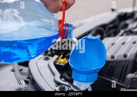 Primo piano il conducente versa il liquido lavavetri blu senza congelamento nel serbatoio della vettura. Foto Stock